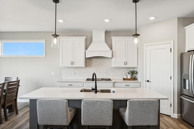 kitchen with premium range hood, pendant lighting, stainless steel refrigerator with ice dispenser, and light countertops