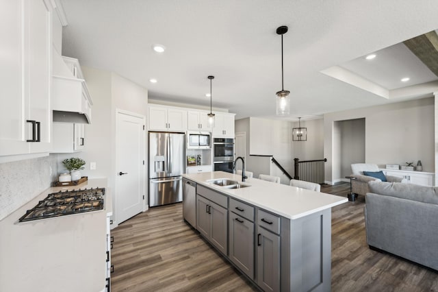 kitchen featuring an island with sink, open floor plan, stainless steel appliances, light countertops, and white cabinetry