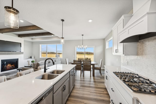 kitchen with custom exhaust hood, stainless steel appliances, light countertops, open floor plan, and a sink