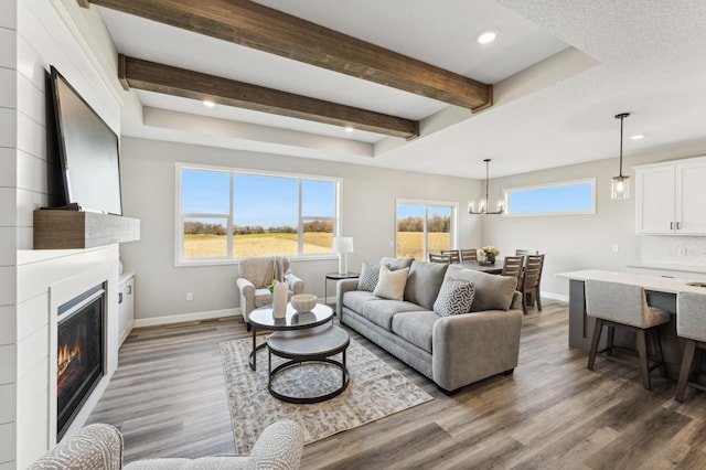 living room featuring dark wood-style floors, an inviting chandelier, a glass covered fireplace, beamed ceiling, and baseboards