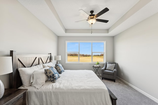 carpeted bedroom featuring a ceiling fan, a raised ceiling, and baseboards