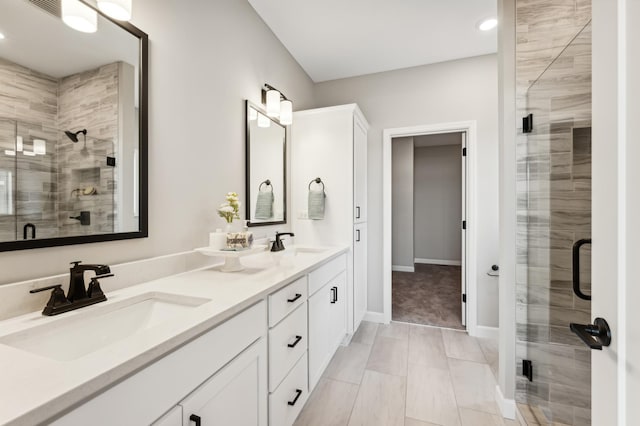 full bathroom with double vanity, a stall shower, baseboards, and a sink