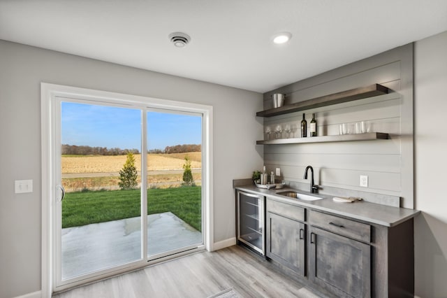 bar with light wood finished floors, beverage cooler, baseboards, a sink, and indoor wet bar