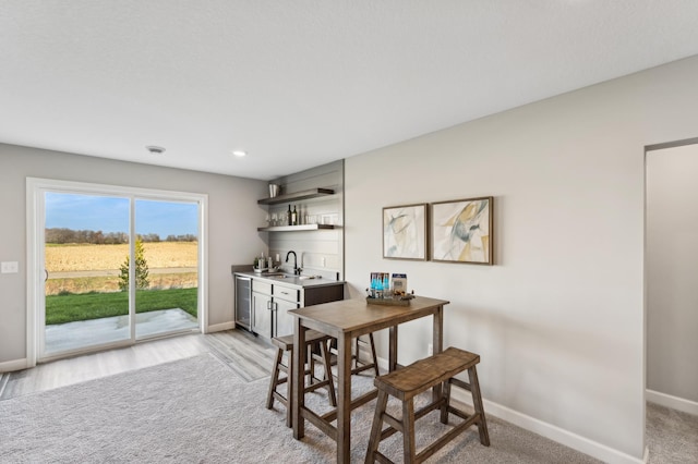 dining space featuring light wood-type flooring, wine cooler, indoor wet bar, and baseboards