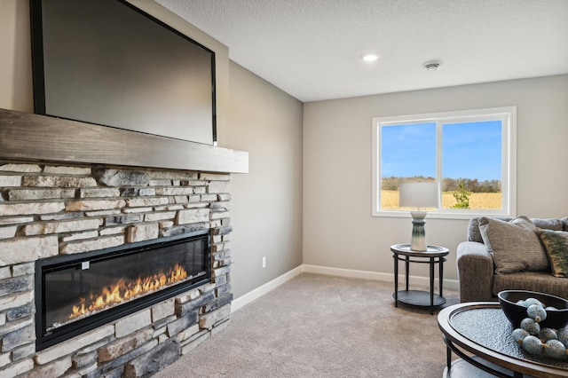 living area featuring baseboards, a stone fireplace, a textured ceiling, and light colored carpet