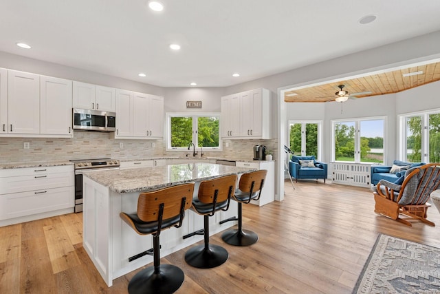 13380 Willandale Rd, Rogers, MN 55374 - kitchen with appliances with stainless steel finishes, a sink, a kitchen breakfast bar, light wood finished floors, and backsplash
