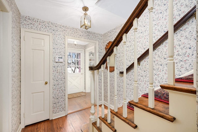 entryway featuring wallpapered walls, stairs, baseboards, and wood finished floors