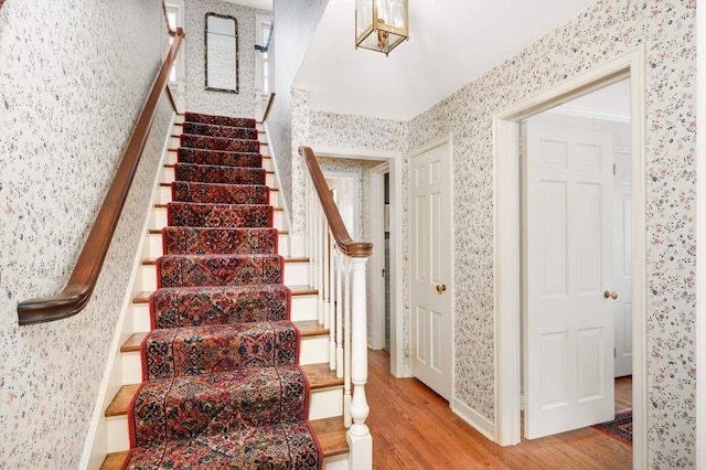 stairs featuring wood finished floors and wallpapered walls