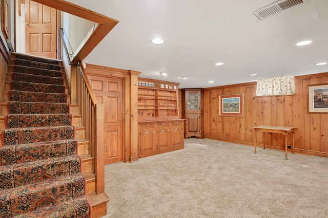 finished below grade area featuring recessed lighting, light colored carpet, visible vents, wood walls, and stairs