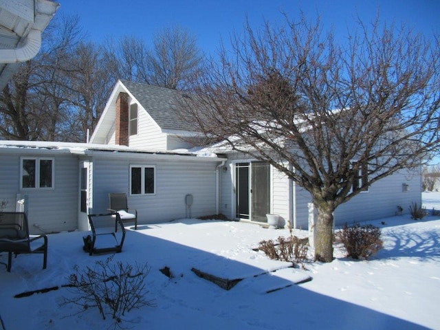 snow covered rear of property featuring a garage and roof with shingles