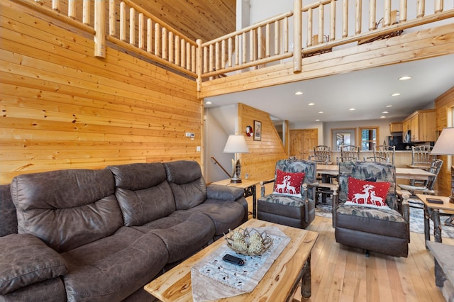 living area with light wood-type flooring, wood walls, a high ceiling, and recessed lighting