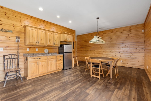 kitchen with dark wood finished floors, decorative light fixtures, freestanding refrigerator, light brown cabinetry, and wood walls