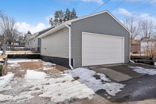 snow covered garage featuring fence and a garage