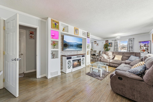 living area featuring crown molding, visible vents, a glass covered fireplace, a textured ceiling, and wood finished floors