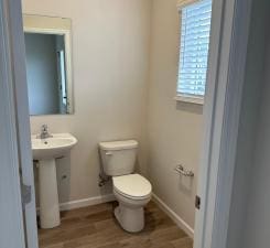 half bath featuring a sink, wood finished floors, toilet, and baseboards