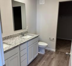 bathroom with double vanity, toilet, a sink, wood finished floors, and baseboards