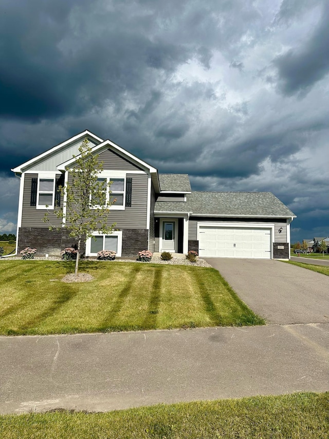 tri-level home with aphalt driveway, a garage, stone siding, roof with shingles, and a front yard