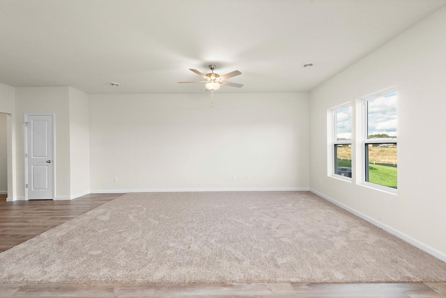 spare room featuring dark colored carpet, ceiling fan, and baseboards