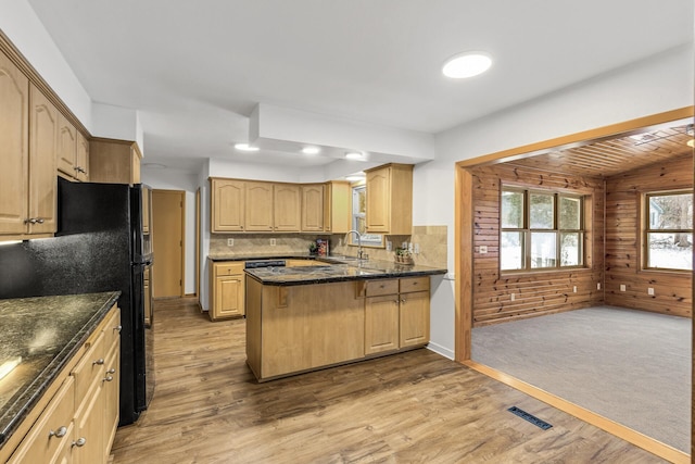 kitchen featuring light wood-style flooring, a peninsula, wood walls, freestanding refrigerator, and light brown cabinetry