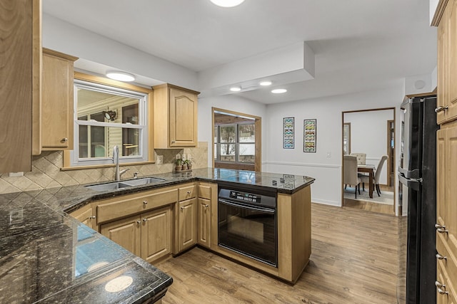 kitchen featuring a peninsula, a sink, light wood-style floors, backsplash, and black appliances