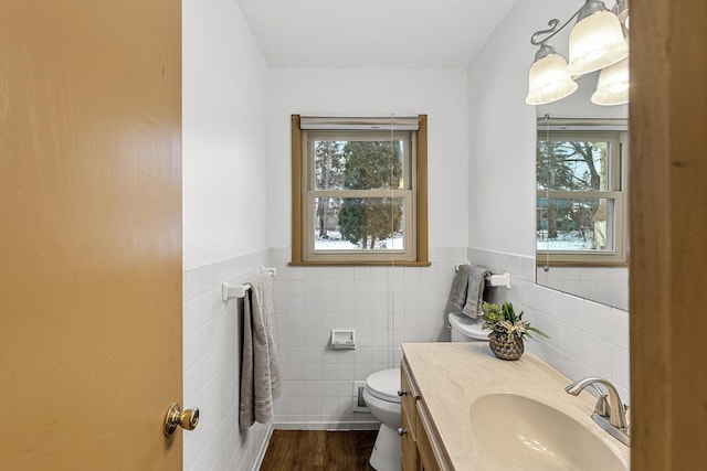 bathroom featuring a wainscoted wall, tile walls, toilet, vanity, and wood finished floors