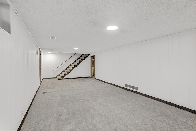 finished basement featuring stairs, a textured ceiling, visible vents, and light colored carpet