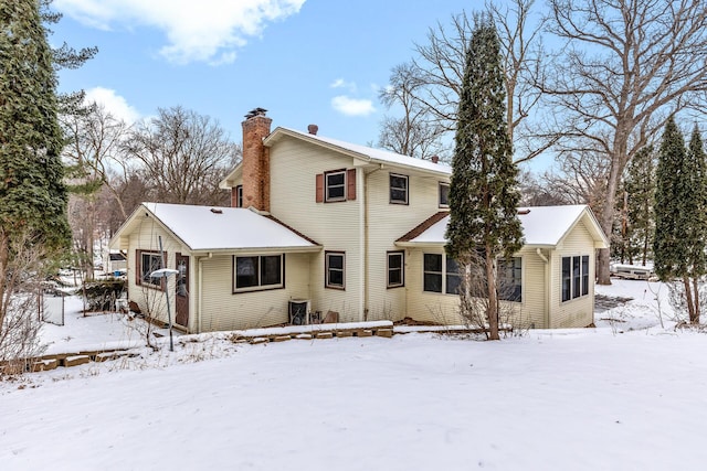 snow covered rear of property with a chimney