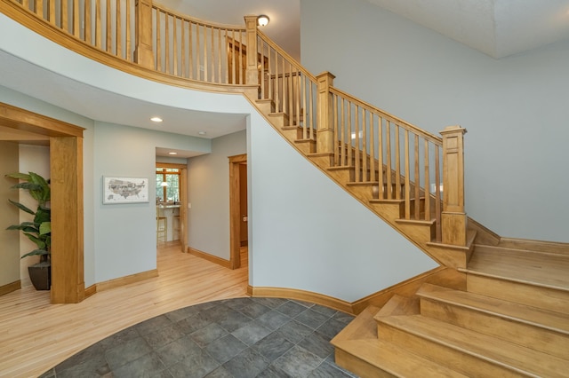 stairs with a towering ceiling, baseboards, and wood finished floors