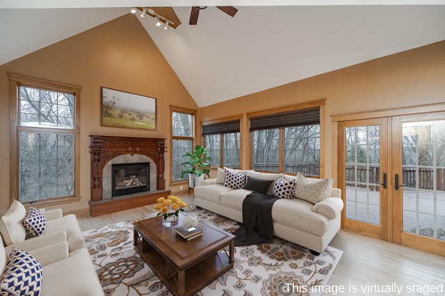 living area featuring french doors, rail lighting, light wood-style floors, a glass covered fireplace, and high vaulted ceiling