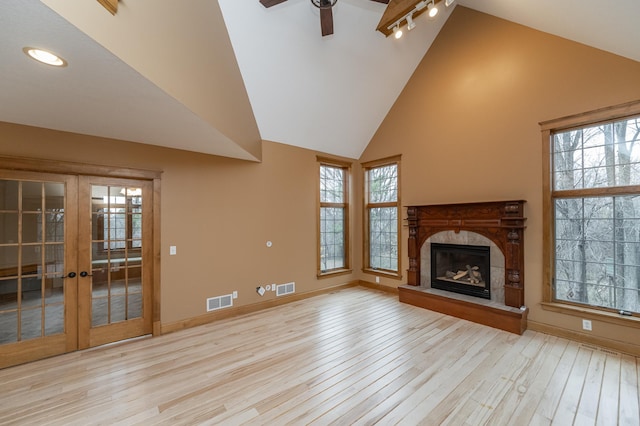 unfurnished living room with high vaulted ceiling, wood finished floors, visible vents, baseboards, and a glass covered fireplace