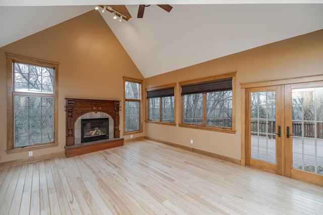 unfurnished living room with light wood-style floors, a glass covered fireplace, track lighting, high vaulted ceiling, and baseboards