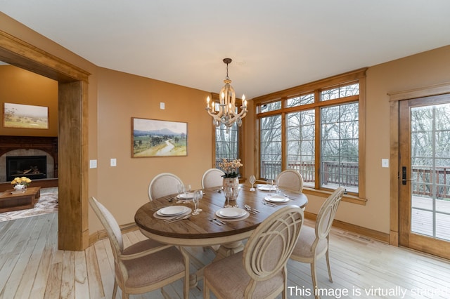 dining space with light wood-type flooring, a fireplace, baseboards, and a notable chandelier