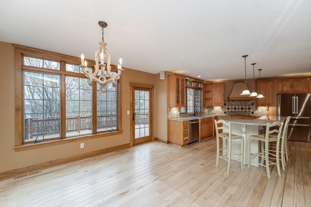 kitchen featuring brown cabinets, appliances with stainless steel finishes, light wood-style floors, a sink, and premium range hood