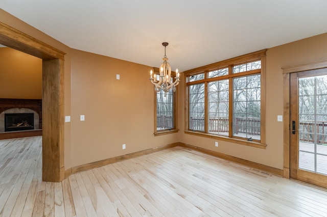 unfurnished dining area with baseboards, visible vents, light wood-style flooring, a fireplace, and a chandelier