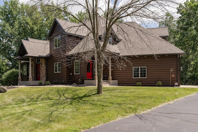 cabin with a shingled roof, a front yard, and stone siding