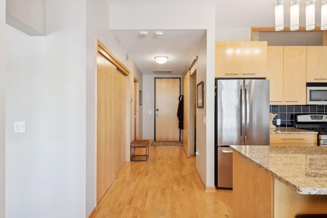 kitchen with light stone counters, stainless steel appliances, light brown cabinetry, pendant lighting, and backsplash