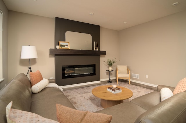 living room with wood finished floors, a glass covered fireplace, visible vents, and baseboards