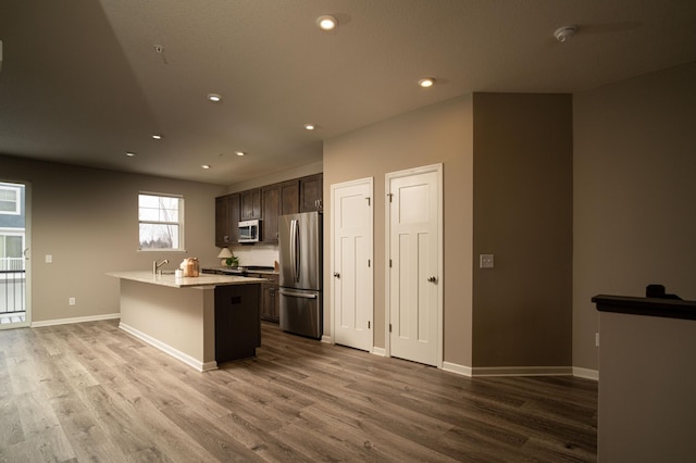 kitchen featuring dark brown cabinetry, a breakfast bar area, a kitchen island with sink, stainless steel appliances, and light countertops