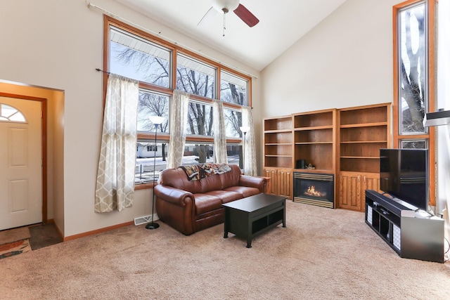 living room featuring light carpet, visible vents, a ceiling fan, a glass covered fireplace, and high vaulted ceiling