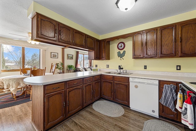 kitchen featuring light countertops, white dishwasher, a sink, wood finished floors, and a peninsula