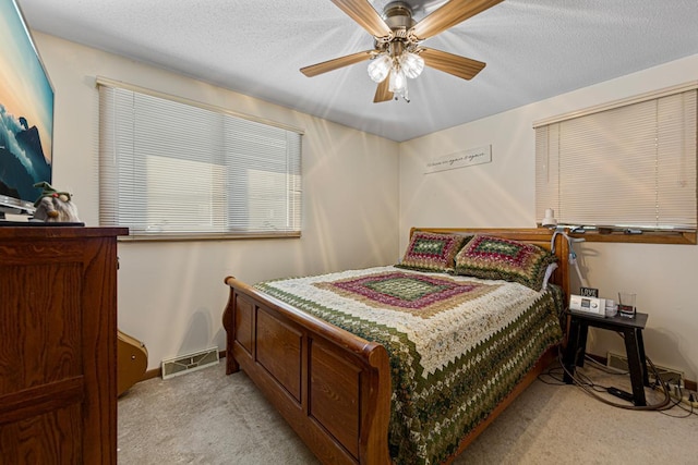 bedroom featuring baseboards, visible vents, a ceiling fan, light colored carpet, and a textured ceiling