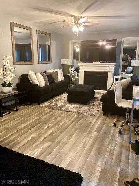 living room featuring a ceiling fan, a fireplace, and wood finished floors