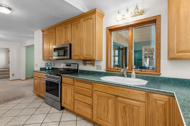 kitchen with a textured ceiling, light tile patterned flooring, stainless steel appliances, a sink, and dark countertops