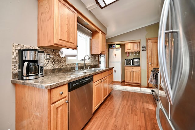 kitchen with lofted ceiling, a sink, appliances with stainless steel finishes, light wood-type flooring, and tasteful backsplash