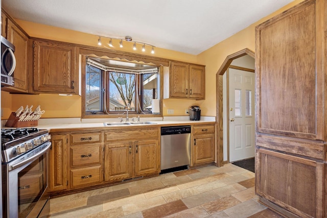 kitchen with arched walkways, light countertops, appliances with stainless steel finishes, and a sink