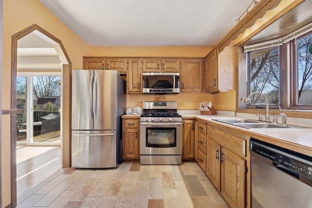 kitchen with arched walkways, light countertops, appliances with stainless steel finishes, brown cabinetry, and a sink