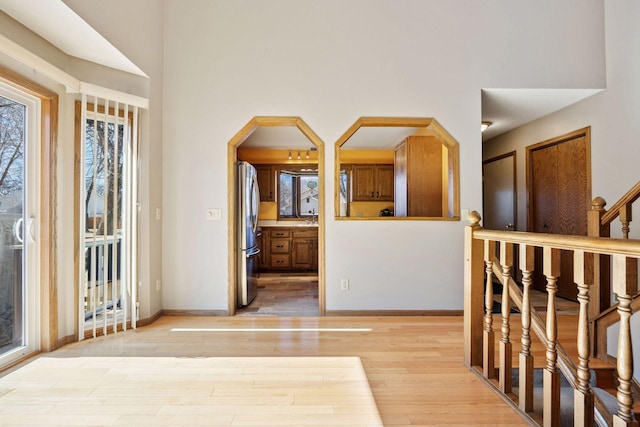 foyer with light wood-type flooring, arched walkways, a high ceiling, and stairs