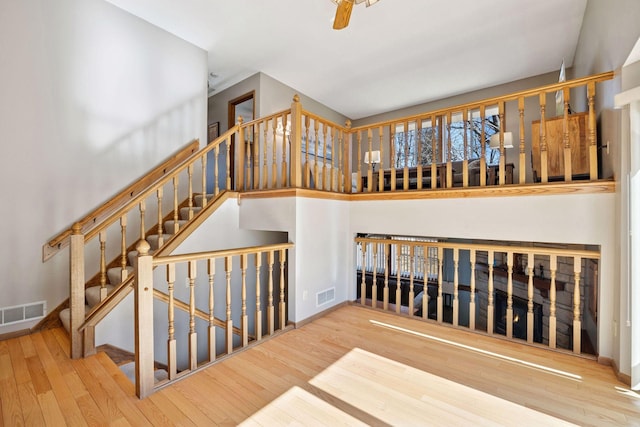 staircase with a ceiling fan, visible vents, baseboards, and wood finished floors