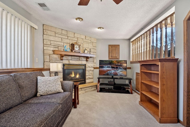 living area with carpet floors, visible vents, ceiling fan, a stone fireplace, and a textured ceiling