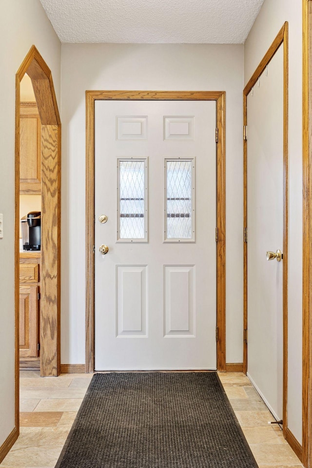 doorway with light wood-style floors, baseboards, arched walkways, and a textured ceiling